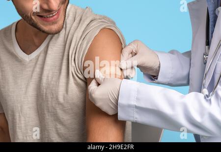 Doctor Applying Sticking Plaster On Young Man's Shoulder After Vaccine Injection Shot Stock Photo