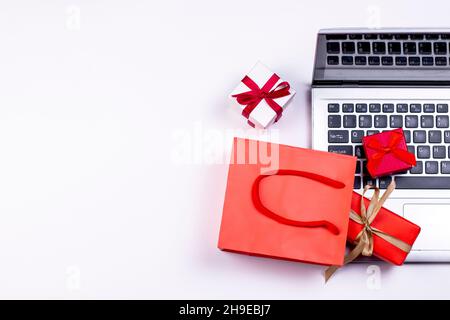 Online shopping concept. Laptop, red paper bag and gift boxes on white background. Stock Photo