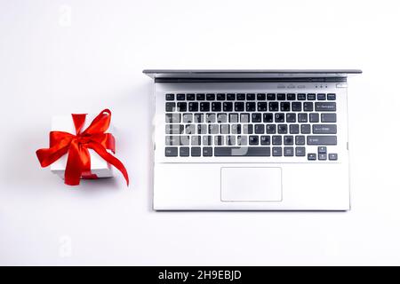 Old laptop and gift box with red ribbon on white background. Used silver notebook and present. Stock Photo