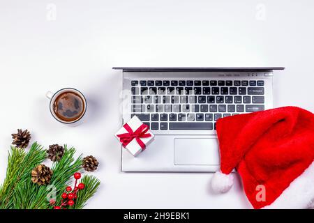 Old laptop with coffee cup, Christmas gift and fir branches with fir cones on white background. Christmas decoration with used silver notebook. Stock Photo