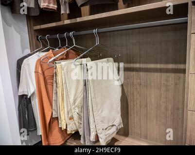 A large, walk in closet with shirts and khaki pants hanging up on hangers Stock Photo