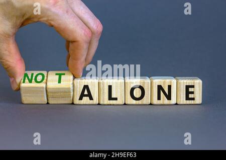 You are not alone symbol. Businessman turns wooden cubes and changes words alone to not alone. Beautiful grey table grey background, copy space. Busin Stock Photo