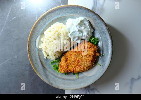 Mediterranean pork chop milanese with risotto and cucumber yogurt dipping sauce served on bed of arugula greens Stock Photo
