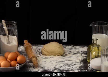 The finished kneaded dough lies on the table, chicken eggs in a plate and sugar and butter Stock Photo