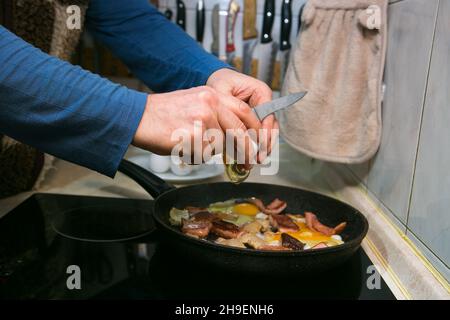 The process of cooking scrambled eggs with lard and sausage. The man prepares two portions. The man fries bacon and sausage in a pan and adds eggs to Stock Photo