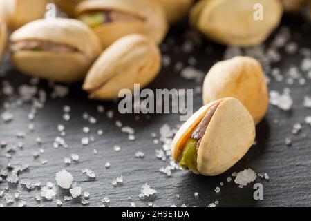 Macro of salted, roasted green pistachio nuts snack on black background with sea salt, healthy food snack, selective focus Stock Photo