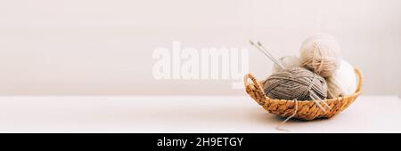 Natural wool in balls of various pastel colors in a wicker basket. Knitting threads close-up on a light background. Stock Photo