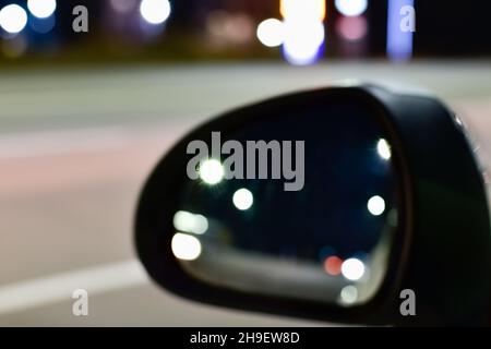 Defocused image of car side mirror on background of illuminated road in evening Stock Photo