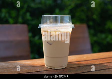 Iced coffee in a plastic mug on a wooden table in the garden. Stock Photo