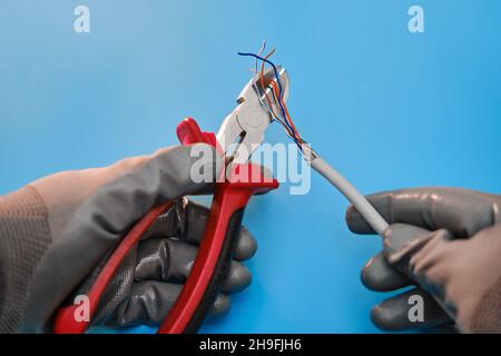 Cutting a computer network wire with wire cutters, blue studio background Stock Photo