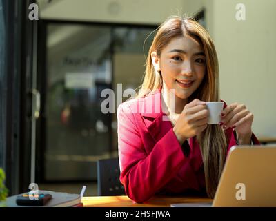 Close-up, Beautiful Asian young businesswoman sips a shot of espresso to start her day at her desk. Stock Photo