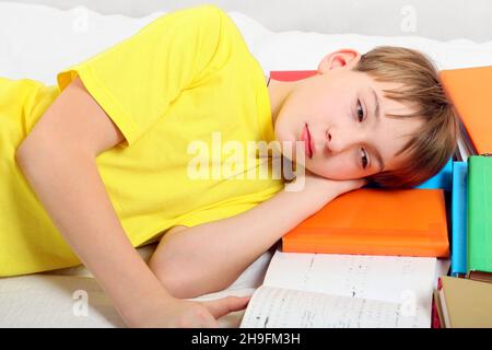 Sad and Tired Kid with the Books on the Bed Stock Photo