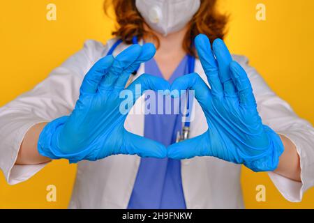 The medic shows the heart sign with his fingers, close-up. Doctor hands in medical gloves with the sign of love for patients, concept Stock Photo