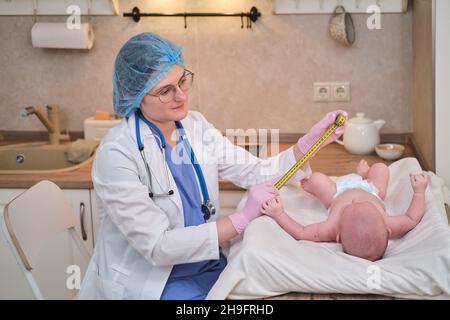 Doctor measures the growth of a newborn baby. A nurse in uniform checks the girth of the child head and abdomen Stock Photo