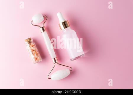 Beautiful composition of unbranded serum bottle, pink himalayan salt and quarts stone face roller on pink background. Anti-ageing cosmetics concept. C Stock Photo
