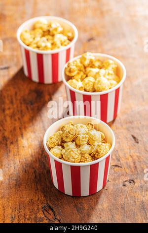 Sweet caramel popcorn in paper cup on wooden table. Stock Photo