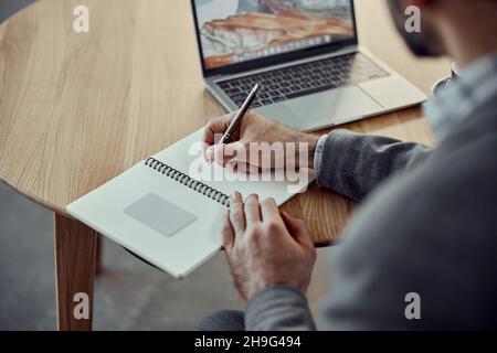 Young man using laptop and writing in notebook Stock Photo