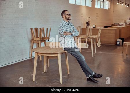 Joyful man sitting on the edge of table in cafe Stock Photo
