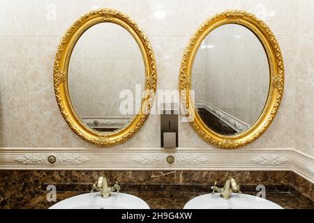Two modern ceramic washbasins with mirrors in the restroom of the restaurant. Ceramic sink with bronze mixer in contemporary toilet . Interior of Euro Stock Photo