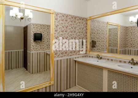 Two modern ceramic washbasins with mirrors in the restroom of the restaurant. Ceramic sink with bronze mixer in contemporary toilet . Interior of Euro Stock Photo