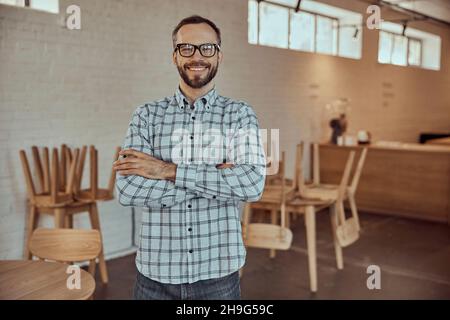 Cheerful bearded man in glasses standing in cafe Stock Photo