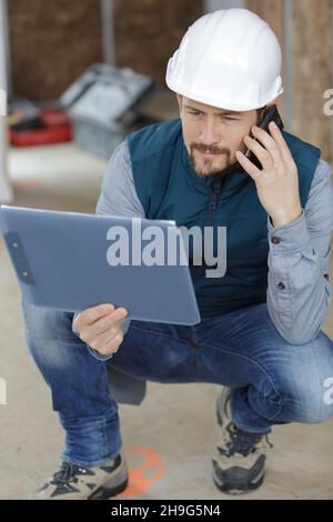 constructor reading something from clipboard notes and talking on telephone Stock Photo