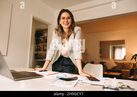 Interior designer working in her home office. Creative businesswoman smiling at the camera while standing behind her desk. Happy female designer plann Stock Photo