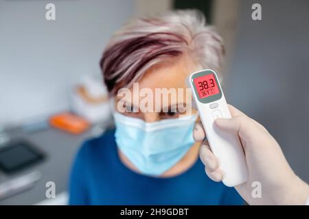 Senior woman with a fever whose temperature is taken by her female doctor Stock Photo