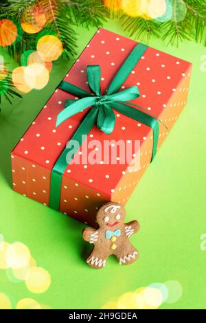 Red rectangular in polka dots wrapped box with gingerbread man on green background with Christmas lights. Gift under Xmas tree. Xmas festive decoratio Stock Photo