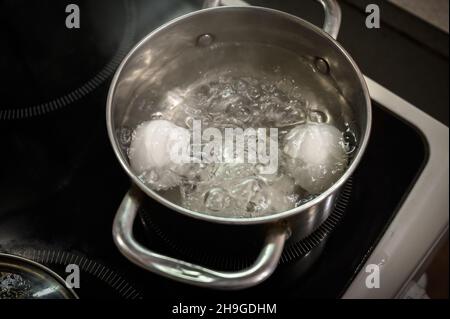 Two white eggs are boiled in a saucepan. Stock Photo