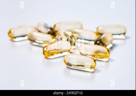 Golden yellow soft capsules reflecting light on white background. Medicine, drug, dietary or nutritional supplement concept. Stock Photo