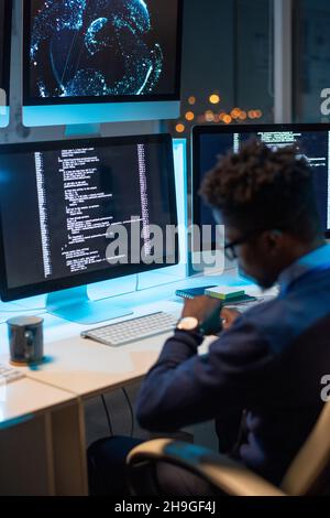 Busy young programmer of African ethnicity looking at wristwatch while working late in the evening in office Stock Photo