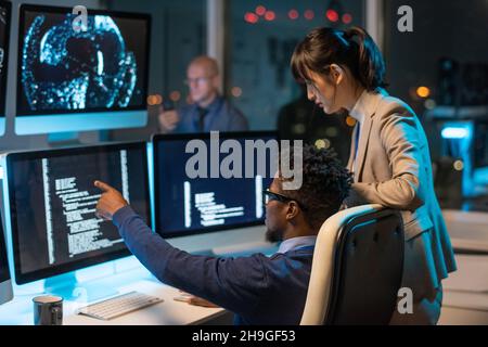Confident businessman pointing at coded data on computer screen while explaining it to female colleague at meeting Stock Photo
