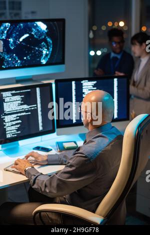 Bald mature businessman decoding data on computer screen while working overtime in office Stock Photo