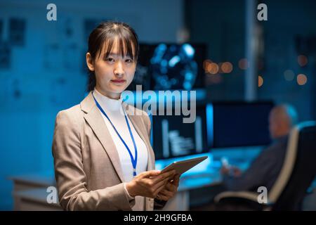 Young serious female programmer or developer in formalwear holding tablet while networking in office environment Stock Photo
