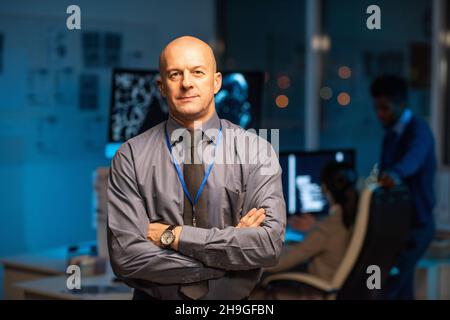 Mature successful manager of company in formalwear crossing arms by chest while standing against his subordinates Stock Photo