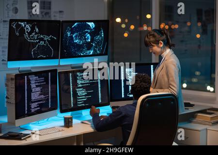 Two intercultural programmers consulting about working points while decoding data on computer screen in office Stock Photo