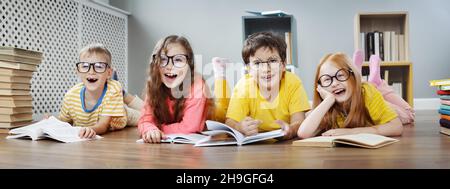 Four cute children in glasses lying on the floor indoors with books Stock Photo