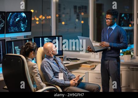 Young successful businessman with laptop making presentation for colleagues at working meeting in office Stock Photo