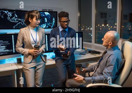 Two businessmen with smartphones and drinks discussing working points while young Asian female colleague listening to them Stock Photo