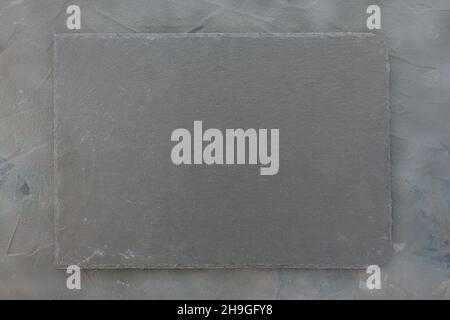 Slate plate on dark gray stone texture background. Kitchen stone tray for serving food. Black granite rectangle board. Empty space for menu or recipe. Top view copy space, mockup Stock Photo