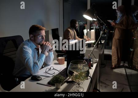Contemporary businessman and his intercultural male and female coworkers staying in office at night Stock Photo