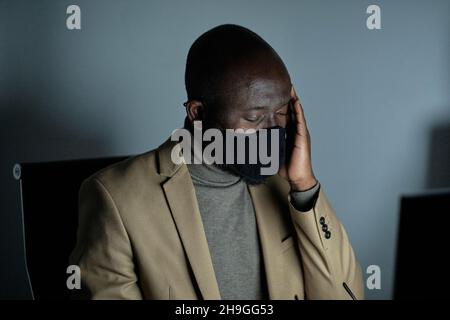 Tired African businessman with headache touching head while working late in the office Stock Photo