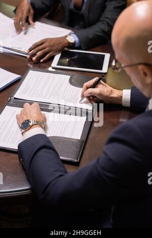 Mature businessman putting his signature on juridical document after reading its terms and conditions Stock Photo