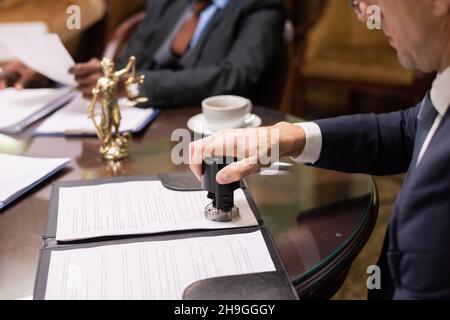Hand of director of large business company putting stamp on document after reading and signing it Stock Photo