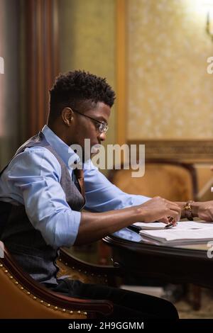 Serious young African male lawayer looking through juridical documents while sitting by table in boardroom Stock Photo
