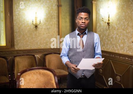 Young confident lawyer with paper standing in boardroom against chairs by walls with lamps Stock Photo