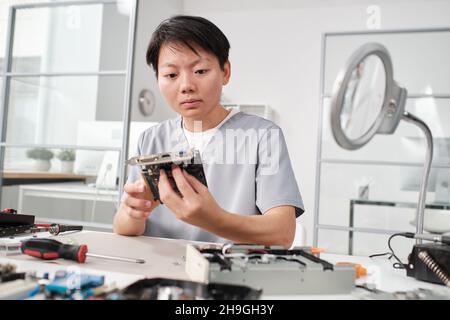 Young serious female specialist checking motherboard or part of computer hardware while sitting by workplace Stock Photo