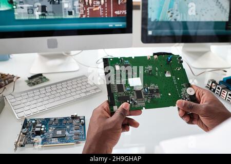 Hands of young African scientist holding part of electronic device with microchips over workplace Stock Photo