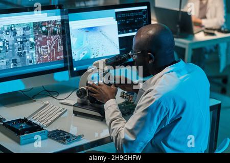 Contemporary young African scientist with microscope working in front of computer monitors Stock Photo